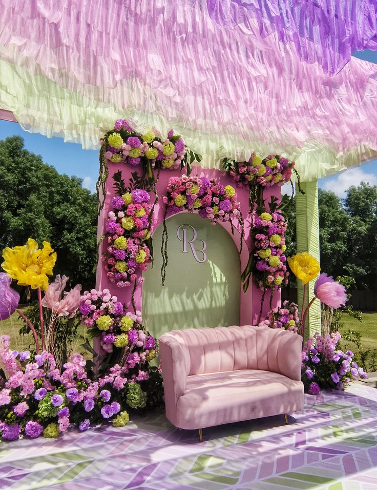 Garden stage with a lilac ruffled canopy, floral arch and pink velvet sofa by RAW Group